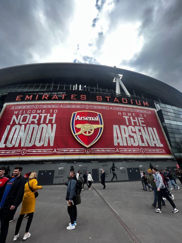 Emirates Stadium exterior Welcome to North London and Home of The Arsenal banner with club crest fans walking outside matchday