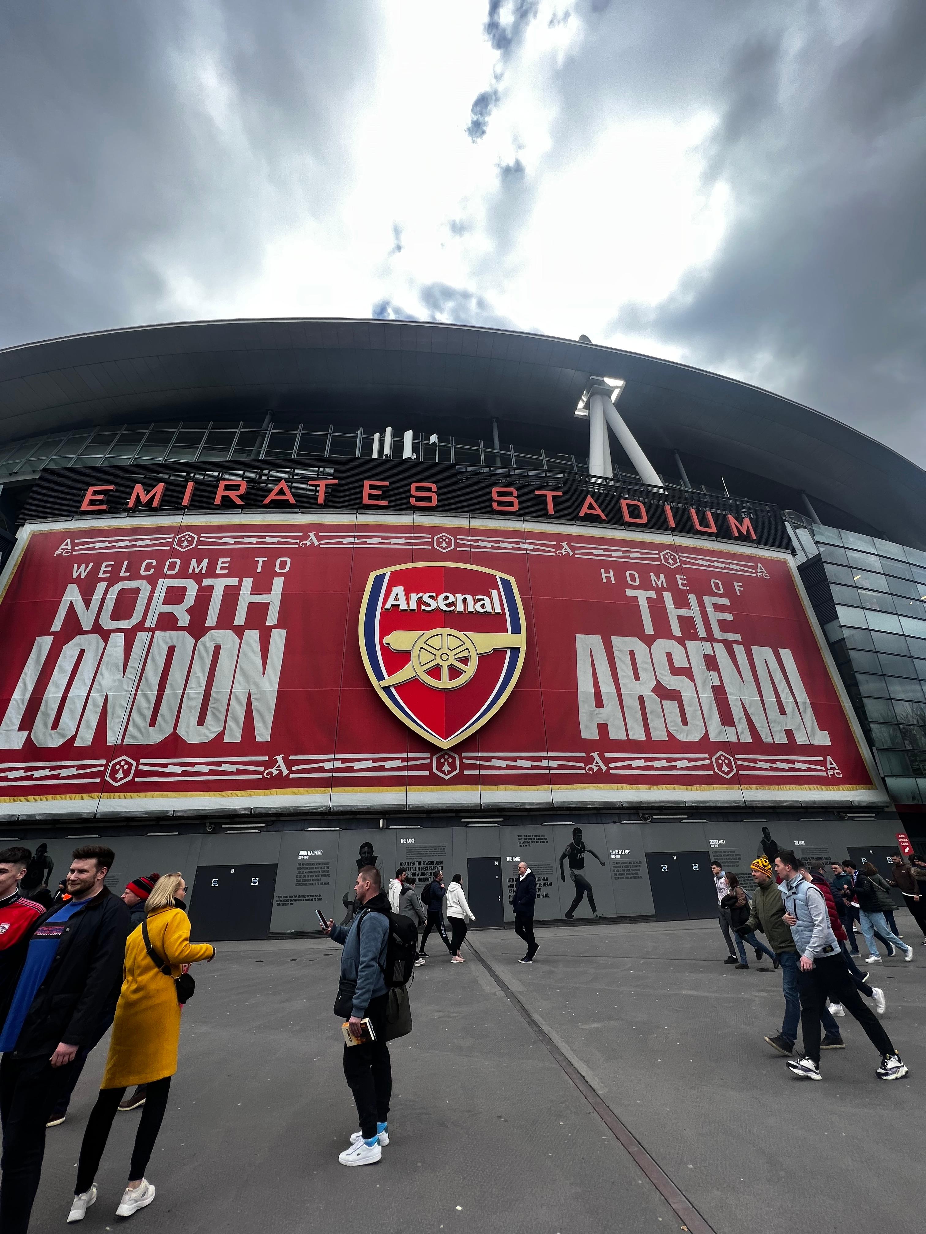 Emirates Stadium exterior Welcome to North London and Home of The Arsenal banner with club crest fans walking outside matchday